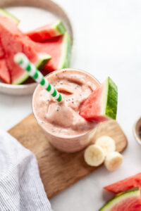 glass of watermelon banana smoothie with a green straw and a piece of watermelon as a garnish