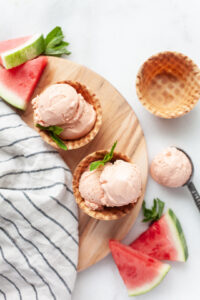 Two waffle cone bowls of Watermelon Ice Cream with watermelon on the side