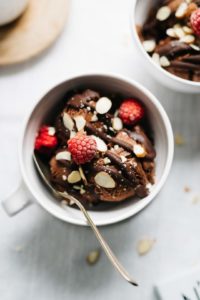 Bowl of chocolate sundae topped with chocolate sauce, raspberries, and almond slivers